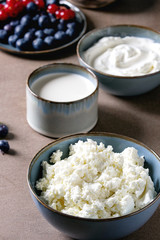 Dairy produce for breakfast. Cottage cheese, plain yogurt, milk, cream, honey, blueberries and red currant berry in ceramic bowl over brown table. Healthy eating. Close up