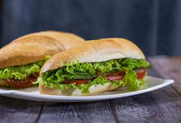 Two fresh underwater sandwiches with sausage, cheese, bacon, tomatoes, lettuce, cucumbers and onions on a dark wooden background