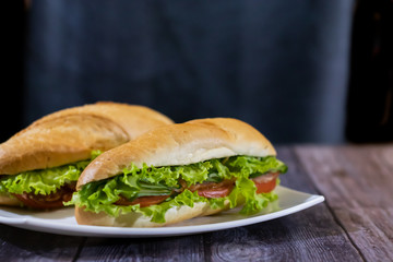 Two fresh underwater sandwiches with sausage, cheese, bacon, tomatoes, lettuce, cucumbers and onions on a dark wooden background
