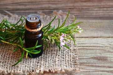 Obraz na płótnie Canvas Rosemary essential oil in a glass dropper bottle with fresh green rosemary herb on old wooden table for spa,aromatherapy and bodycare.Copy space.