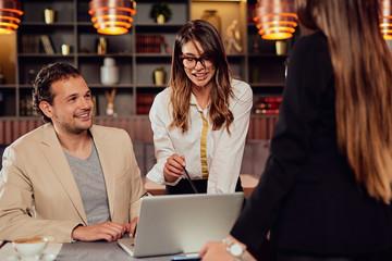 Arrtactive businessman dressed smart casual sitting in cafe. Around him his colleagues standing and  discussing about important project.