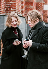 Blond curly-haired guy and the same girl are looking for information in mobile devices