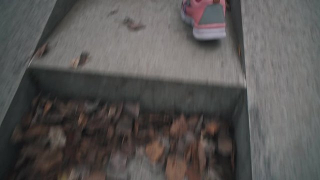 Handheld shoot close up of pink sneakers on children's feet climbs stone steps in dry leaves. Child walks on gray stairways in city park.
