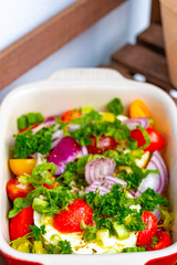 Large portion of ripened Halloumi or Feta cheese with many fresh herbs, tomatoes and red onions in a casserole dish for grilling in the oven or on the grill for a barbecue