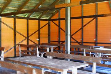 Part of outdoor gazebo with wooden tables and chairs, orange walls and green roof.