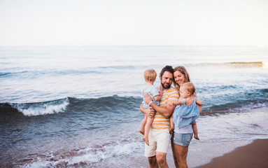 A young family with two toddler children standing on beach on summer holiday.