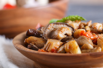 Fried oyster mushrooms with tomatoes in wooden plate on black concrete background. side view.