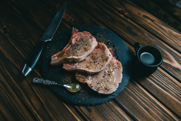 Raw fresh meat Pork steak and seasonings on dark wooden background board slate with honey knife