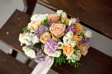 Wedding bouquet of pink roses with a lilac on a blurred background on a wooden staircase