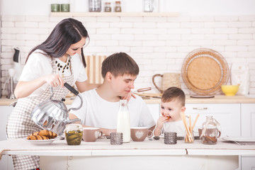 Happy family cooking dinner together. Young parents and their kid having breakfast. People eating on the kitchen.