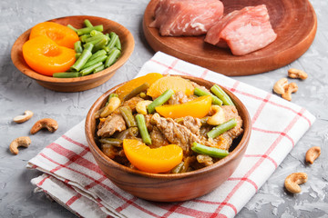 Fried pork with peaches, cashew and green beans on a black concrete background, side view. raw meat, red pepper, linen textile.