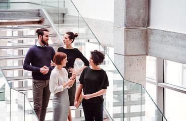 Group of young businesspeople standing near staircase, talking.