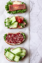 Fresh sandwiches with sausage, cheese, bacon, tomatoes, lettuce, cucumbers on a light background. Vertical orientation