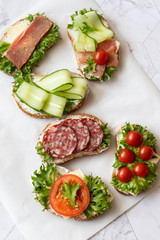 Fresh sandwiches with sausage, cheese, bacon, tomatoes, lettuce, cucumbers on a light background. Vertical orientation