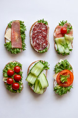 Fresh sandwiches with sausage, cheese, bacon, tomatoes, lettuce, cucumbers on a light background. Vertical orientation