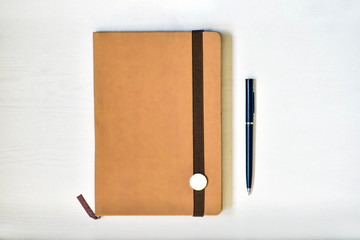 Notebook (beige, brown), lying on a white table, illuminated by natural muted daylight. - 266333578