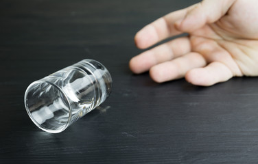 Lying empty glass of vodka or alcoholic drink, hand drunk in the background, concept of alcoholism and alcohol abuse, defocused, selective focus, close-up, black table, dark background