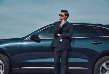Confidence and charisma. Handsome young businessman keeping hand on chin while standing near his...