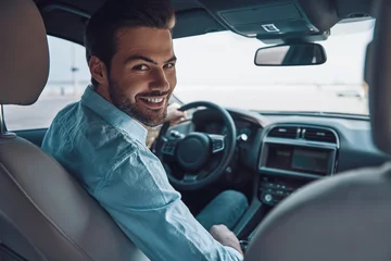 Foto op Canvas Are you ready to go? Rear view of young man in smart casual wear looking at camera over shoulder and smiling while driving a status car © gstockstudio