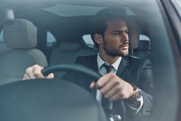 Looking around. Handsome young man in full suit looking away while driving a car