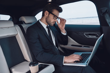Surfing the net. Handsome young man in full suit working using laptop while sitting in the car