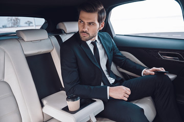 Confident businessman. Handsome young man in full suit looking away while sitting in the car