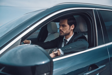 Fototapeta na wymiar Just keep moving! Handsome young man in full suit looking straight while driving a car