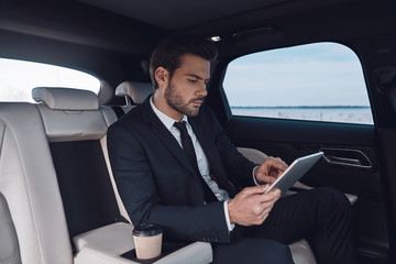 Considering the next step. Handsome young man in full suit working using digital tablet while sitting in the car