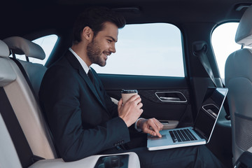 Driven by success. Handsome young man in full suit working using laptop while sitting in the car
