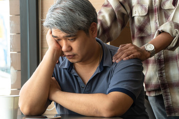 Middle-aged Asian man 40 years old, stressed and tired, are sitting in fast food restaurant and have friends standing behind to encourage. Concept of helping and encouraging