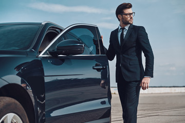 Getting ready to drive. Handsome young businessman entering his car while standing outdoors