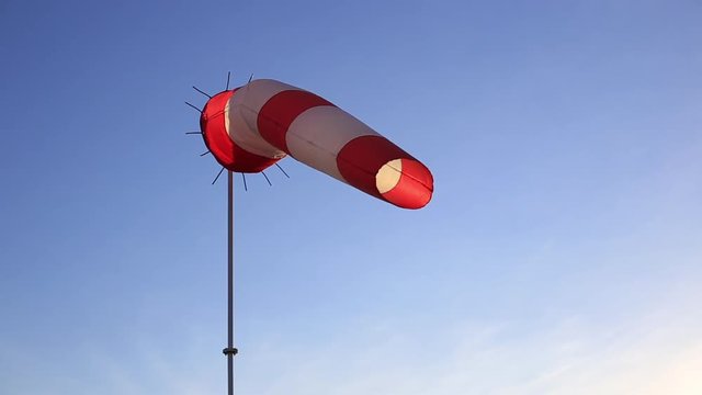 Striped red and white wind vane against a clear blue sky.