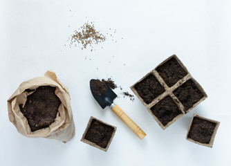 Eco friendly pots for seedlings and seeds on white background, small bag with ground and garden trowel