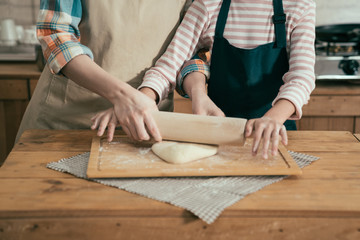 Hands of mother and daughter knead dough for pizza on wooden table. Having fun together in kitchen. unrecognized asian female wife in apron with kid teaching learning baking bread cake for easter.
