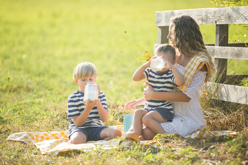 Young pretty mother having picnic with her little children. Family drinking milk outdoors