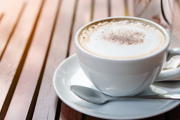 Hot coffee placed on the wooden table in early morning with copyspace, white cup and silver spoon. The green background with defocus effect.