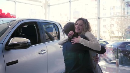 birthday gift, loving male gives new auto to smiling woman which happy hugs and shows keys at auto shop