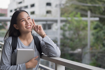 Fototapeta premium portrait of happy smiling asian woman college student thinking and looking up at blank space, city campus environment