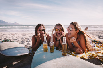 young adult friends laying on beach having fun and drinking beer