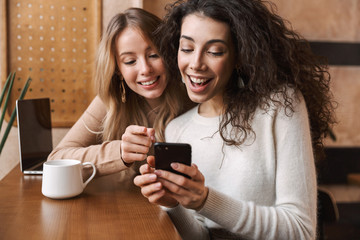 Two cheerful young girlfriends sitting at the cafe