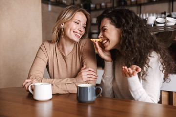 Happy girls friends sitting in cafe talking with each other drinking tea or coffee.