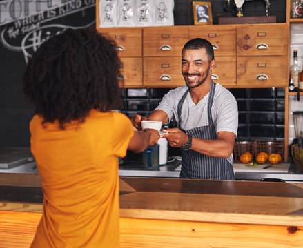 Male barista offers hot coffee to female customer