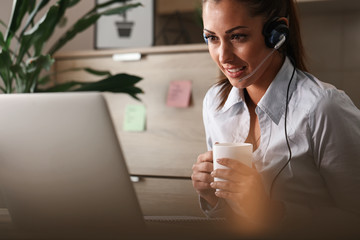 Female call centre agent using laptop while drinking coffee in the office.