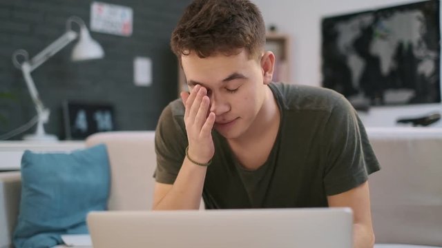 A young boy is working on his laptop when he suddenly gets confused and disappointed