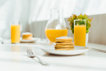 selective focus of sweet pancakes with fresh orange juice in glass served for breakfast on white table