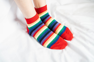 Women's legs in socks colors alternating, side stand on white fabric floor.