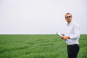 Young agronomist holds tablet touch pad computer in green wheat field. Agribusiness concept. agricultural engineer standing in a wheat field with a tablet in summer