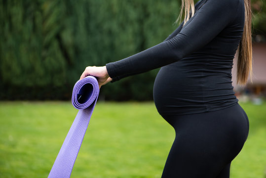 For the baby health. Young pregnant sporty woman standing outdoor holding the gymnastic rug and preparing for exercises.