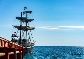 Old sailing pirate ship at the pier, used for tourist trips by sea on the background blue sky and...