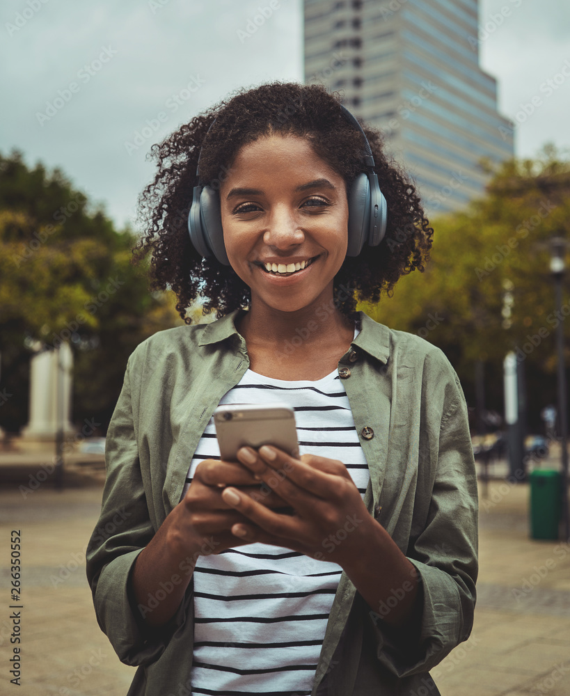 Wall mural Young woman listening to music using smart phone through headphone